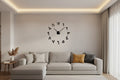 Black wall clock with large numbers on a white wall above a beige sofa with blue pillows.