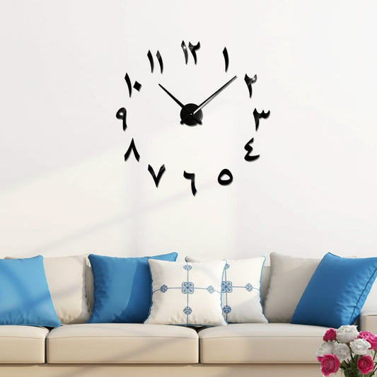 Black wall clock with large numbers on a white wall above a beige sofa with blue pillows.